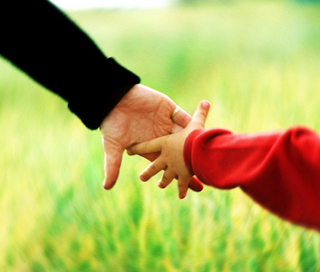 A woman in a black shirt holds hands with a child in a red shirt while walking in a field. A woman in a black shirt holds hands with a child in a red shirt while walking in a field.