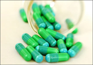 Blue and green antibiotic capsules spilling out of a cup. Blue and green antibiotic capsules spilling out of a cup.
