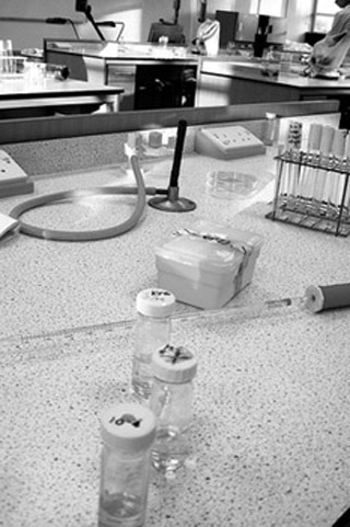 Black and white photo of lab counter with three vials of bacterial cultures and other lab equipment. Black and white photo of lab counter with three vials of bacterial cultures and other lab equipment.
