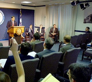 A speaker gives a press conference in a crowded room. A speaker gives a press conference in a crowded room.